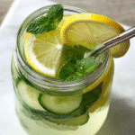 Cucumber Mint Lemonade 2 Top-down view of cucumber mint lemonade in a mason jar with lemon slices, cucumber rounds, and mint leaves on a white marble table