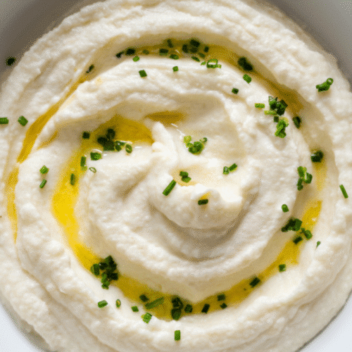 Creamy cheesy mashed cauliflower in a white bowl topped with chives