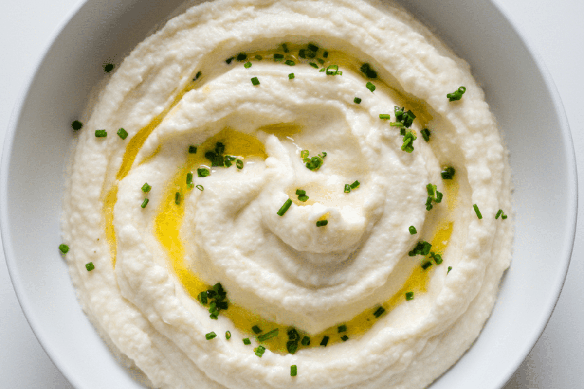 Creamy cheesy mashed cauliflower in a white bowl topped with chives