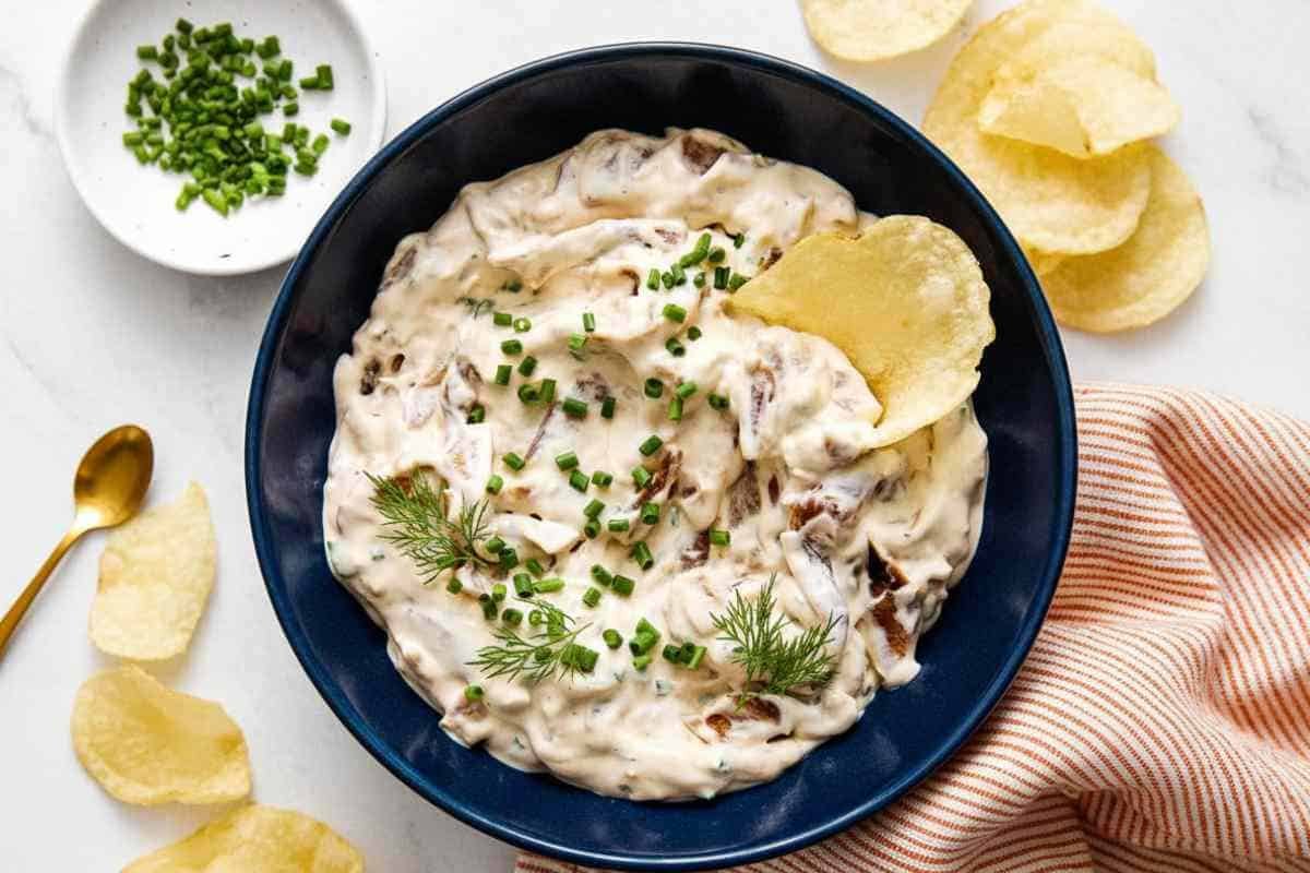 French Onion Dip Recipe Creamy homemade french onion dip in blue bowl topped with fresh chives and caramelized onions, served with potato chips